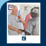 Homme souriant tenant un micro et serrant une main.